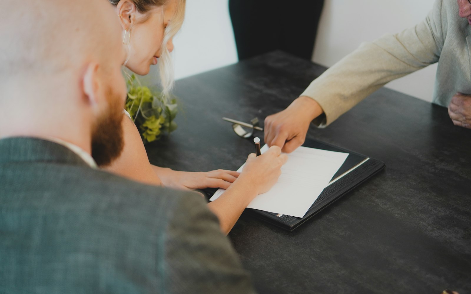 Buyer signing a purchase agreement at a table while the agent points to the document