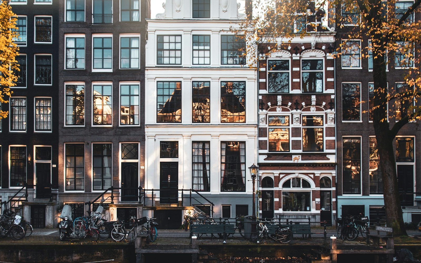 Row of Amsterdam canal houses in autumn, with bicycles and benches along the quay